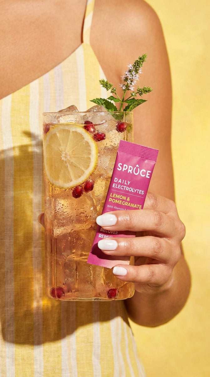 Holding a glass of Lemon & Pomegranate Spruce and a sachet