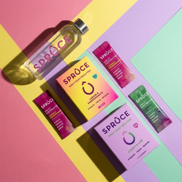 The Electrolyte Month: Lemon & Pomegranate and Cherry & Lime Daily Electrolytes with sachets and the Spruce bottle, flat lay on diagonal colour stripes
