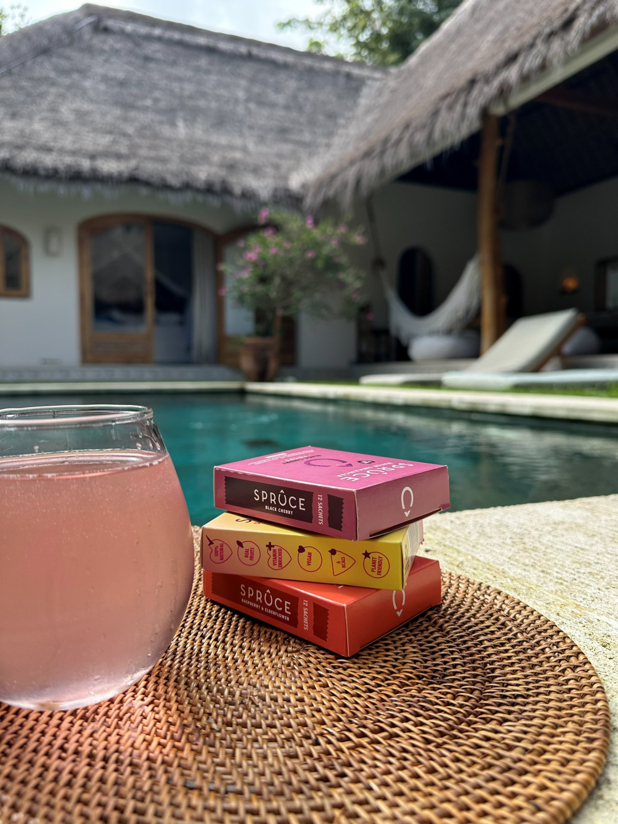 A glass of pink Spruce by a pool beside a stack of Spruce boxes