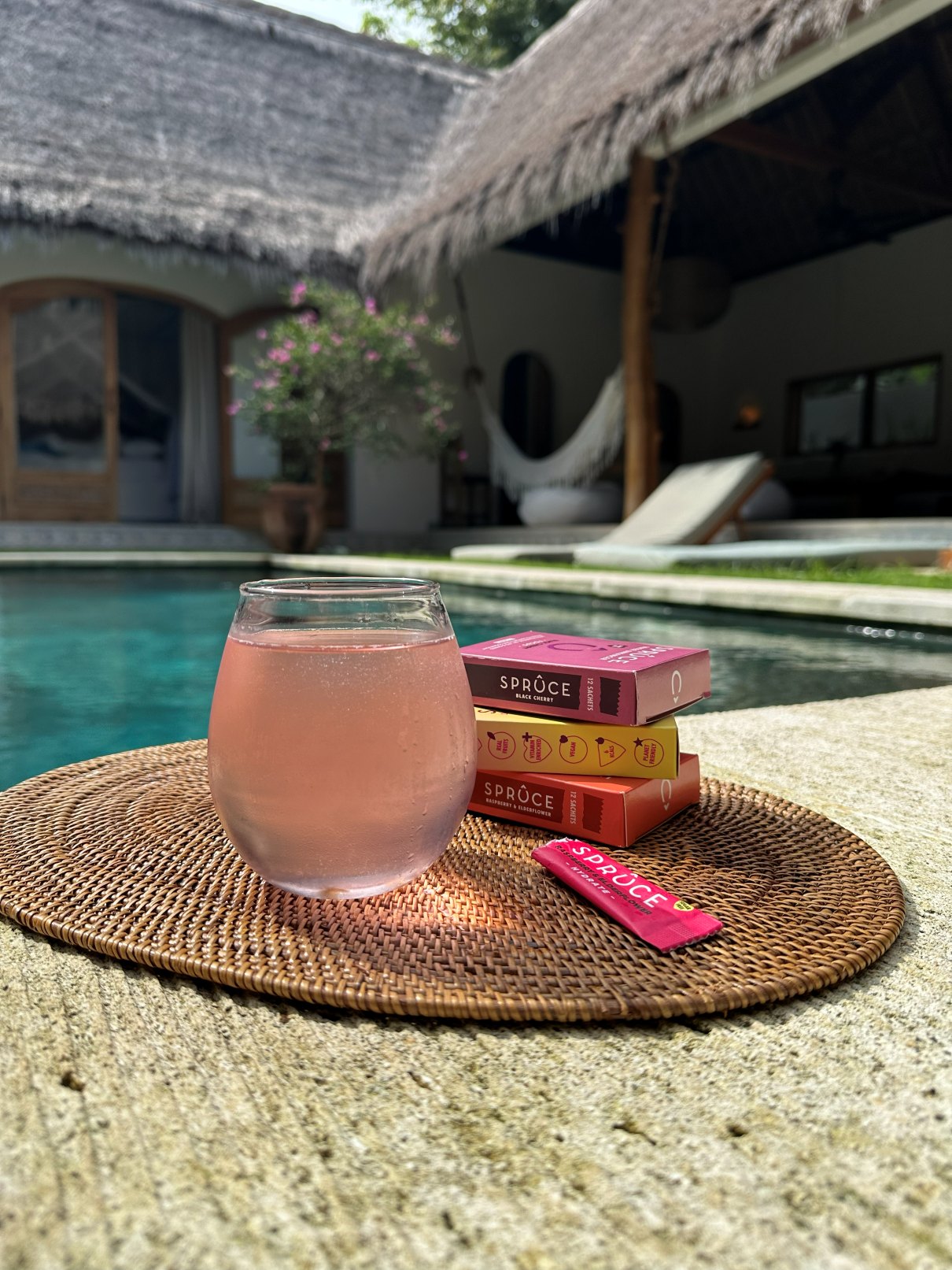 A fizzy glass of pink Spruce by a pool with Spruce boxes and a sachet